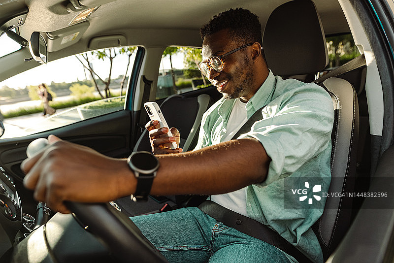 快乐的非洲裔美国人坐在他的车里，使用智能手机图片素材