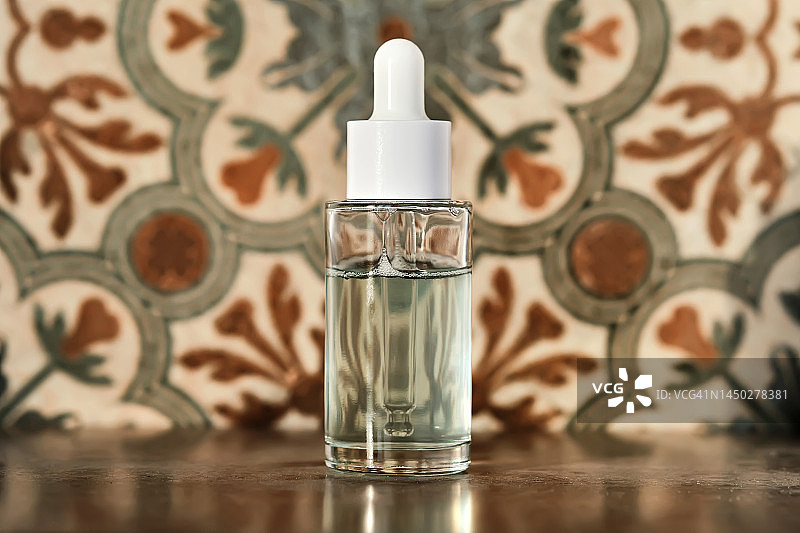 浴室瓷砖背景上的一瓶透明美容精华液。图片素材