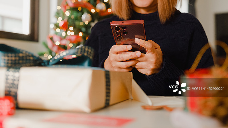 特写妇女手拿智能手机拍照圣诞礼盒在家里的桌子上。图片素材