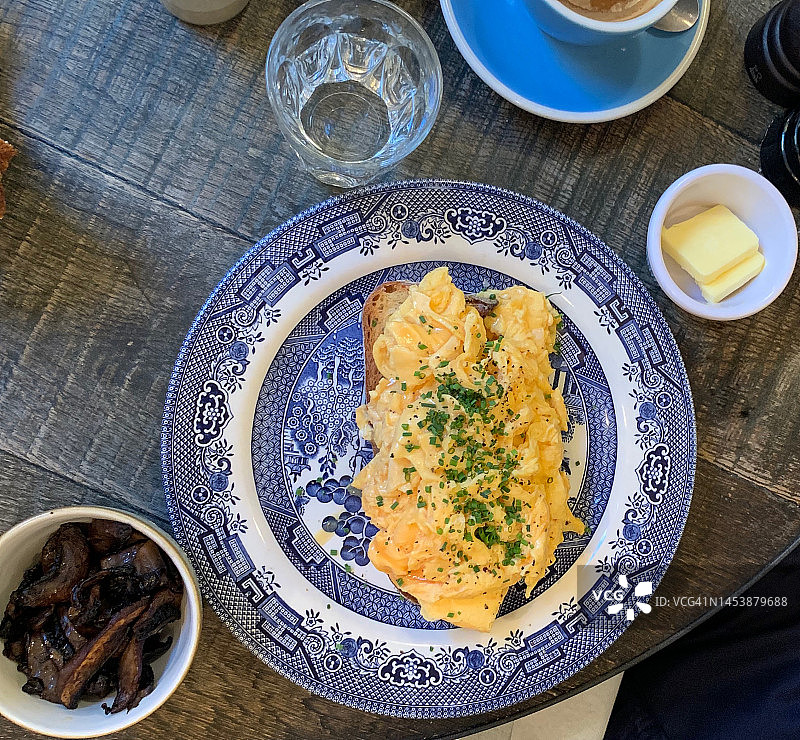 有机炒鸡蛋，手工烤面包，放在古董瓷盘上，配上烤蘑菇和一小块新鲜的根西岛黄油;2022年2月，诺丁山门伦敦时尚小酒馆的早餐桌图片素材