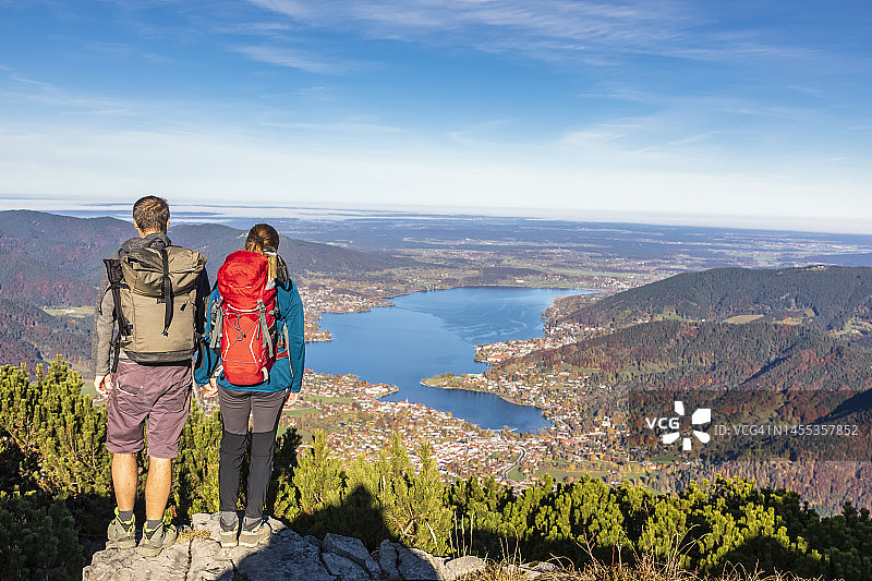 德国，巴伐利亚，罗塔奇-埃格恩，徒步夫妇欣赏泰根塞湖和周围的城镇从瓦尔贝格山的顶峰图片素材