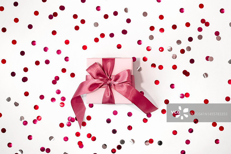 情人节布局:白色礼盒与品红色蝴蝶结的节日背景与红色，粉红色和银色的五彩纸屑。俯视图，平面布局图片素材
