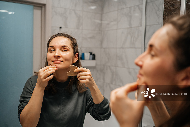 女子在镜子前用瓜沙石做面部按摩图片素材