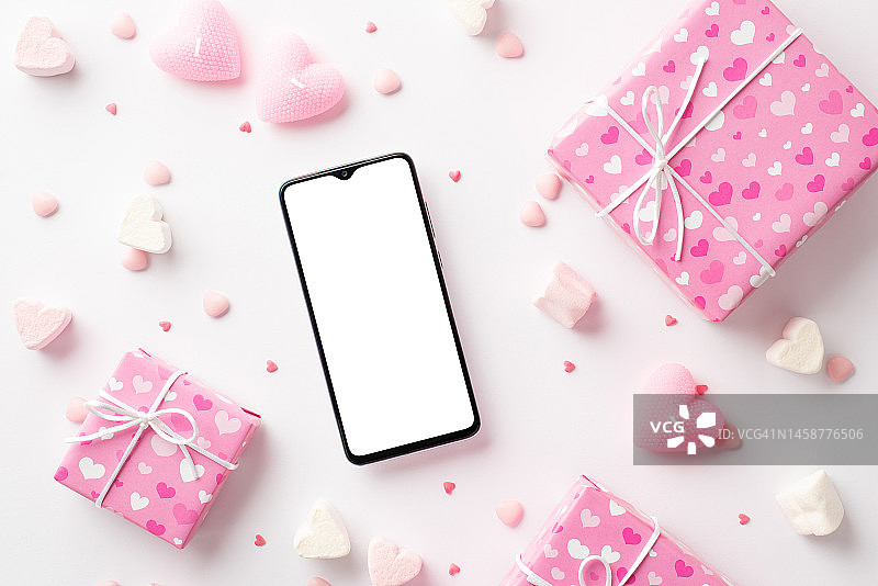 情人节的概念。智能手机粉色礼盒俯视图照片心形棉花糖蜡烛和洒在孤立的白色背景与空白图片素材