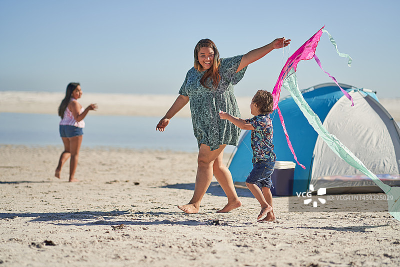 快乐的母亲和儿子在阳光明媚的海滩上玩风筝图片素材