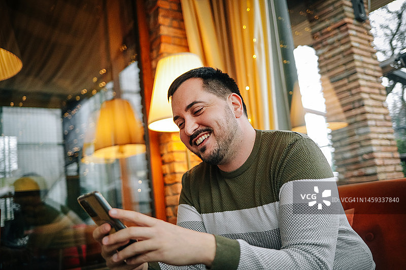 年轻的微笑男子坐在咖啡店和使用电话图片素材