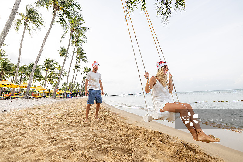 圣诞节期间，一对戴着圣诞帽的夫妇在海滩上玩耍图片素材