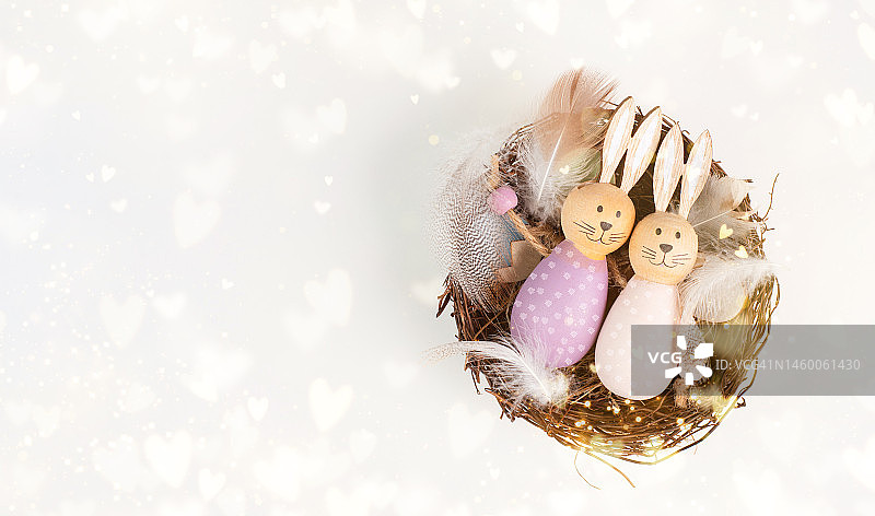 复活节小兔子或小白兔情侣依偎在柳条编成的鸟巢里，用小鸟的羽毛和爱心做成春节贺卡图片素材
