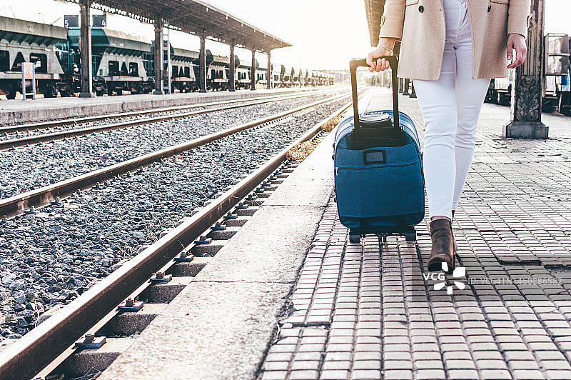一个戴着贝雷帽和米色夹克的女孩的肖像，带着她的行李箱穿过火车站。图片素材