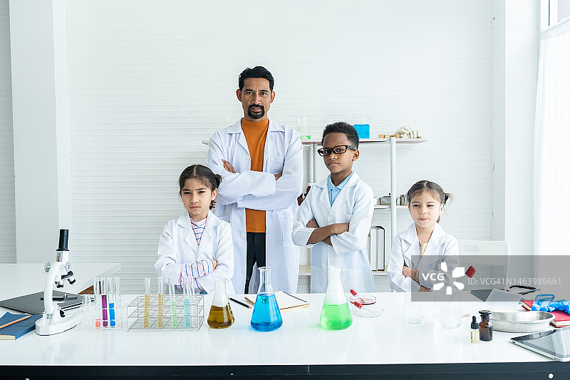 女学生男学生女学生在科学教室里，当实验成功时，他们和科学老师盘腿站在放着试管的桌子前。图片素材