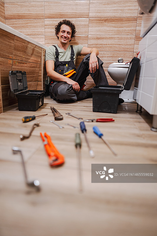 一个水管工坐在浴室地板上解决马桶问题的肖像图片素材