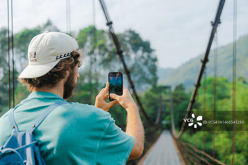 男子用智能手机拍摄丛林吊桥图片素材