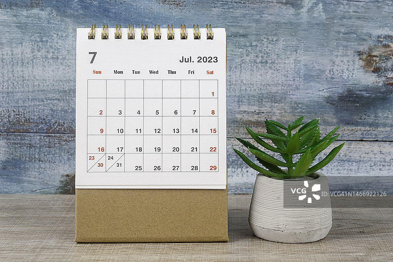 日历桌2023:7月是组织者计划和截止日期的月份，在木桌背景下放置室内植物。图片素材
