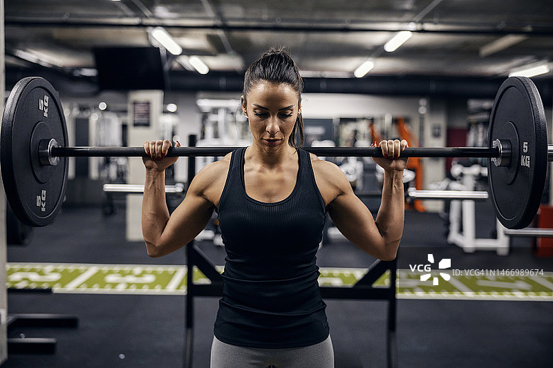 一个肌肉强壮的女健美运动员在健身房举重的肖像。图片素材