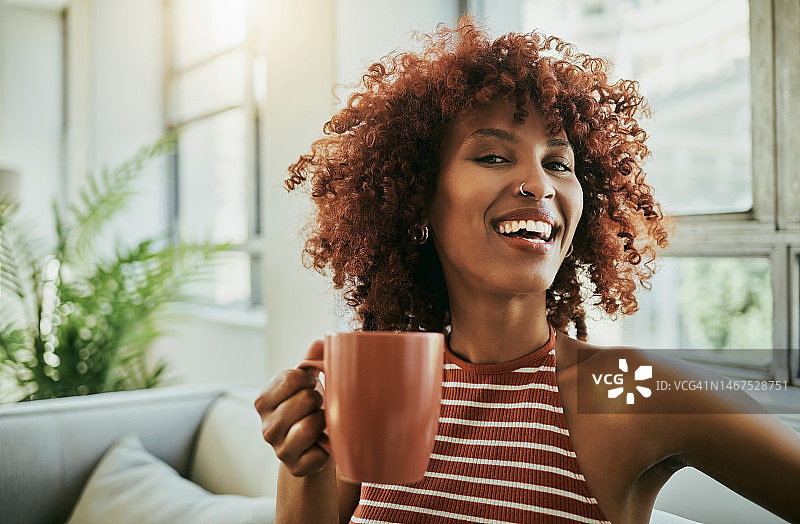 咖啡，快乐和一个女人的肖像在她的客厅在一个周末的早晨例行公事。幸福，微笑，非洲女性在她的现代家庭的沙发上笑着喝卡布奇诺。图片素材