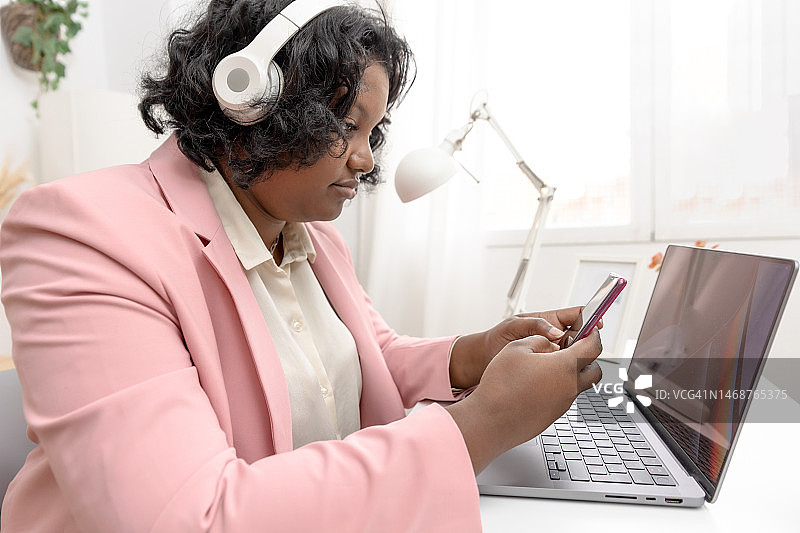 非裔美国女企业家在办公室工作，有笔记本电脑和手机。图片素材