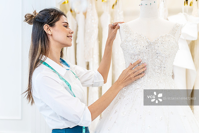 微笑的白人妇女是新娘商店老板，在婚礼工作室的办公室里整理婚纱，小企业企业家婚礼策划师和裁缝设计师概念图片素材