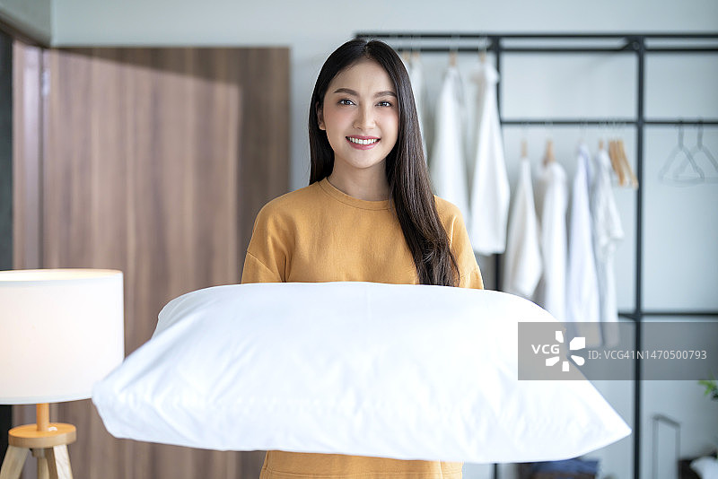 快乐的亚洲年轻成年女性，早上在家里公寓的窗户上，她自己设置了床单和毯子图片素材