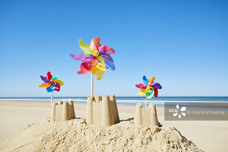 沙滩上有彩色风车的沙堡，衬着大海和蓝天图片素材