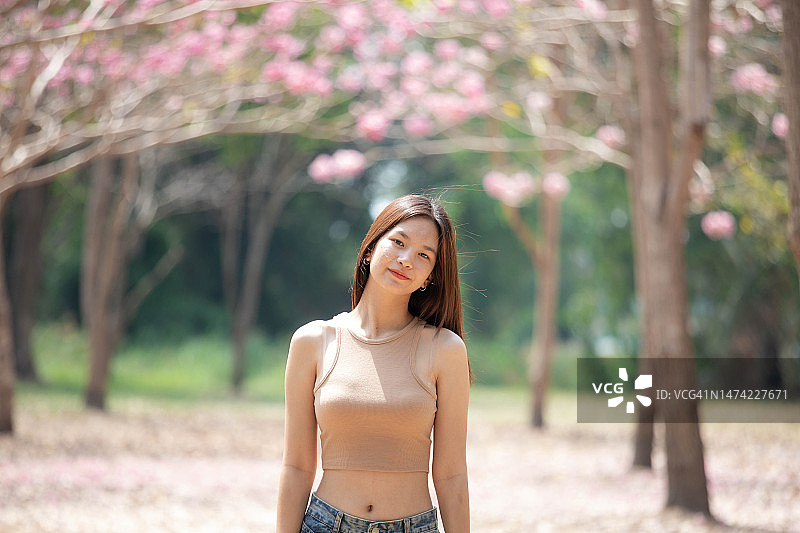 亚洲年轻快乐的女人在公园里盛开的樱桃树前图片素材
