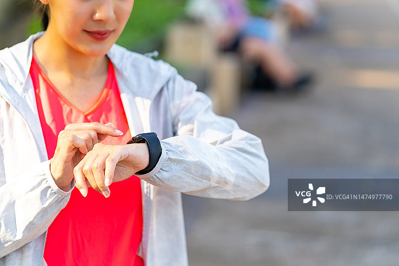 亚洲女子早上在公园慢跑时使用智能手表。图片素材