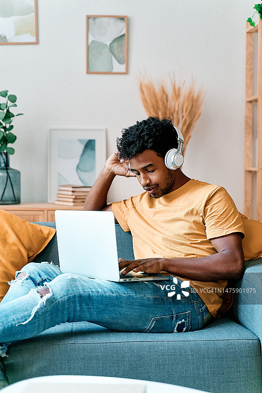 年轻人坐在沙发上用笔记本电脑听音乐图片素材