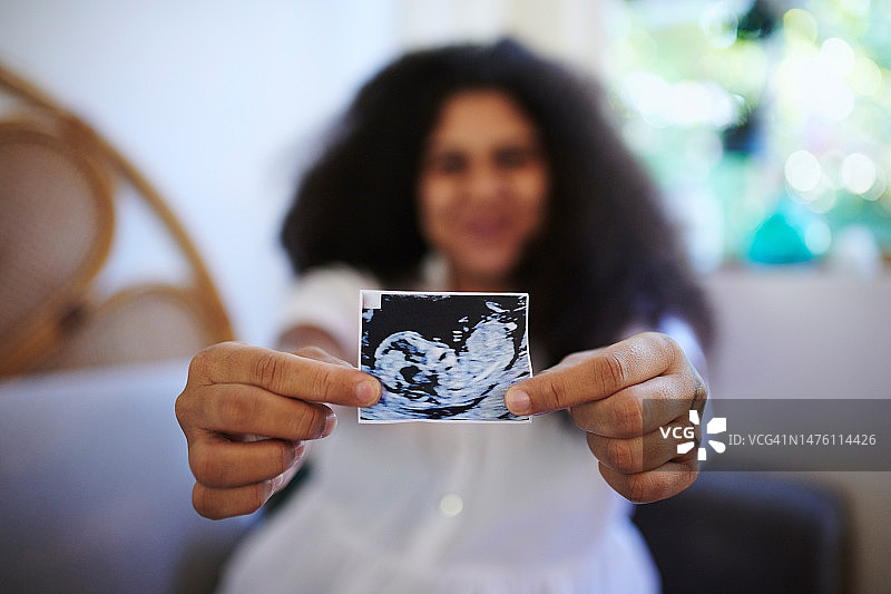 怀孕，显示和手的妇女与超声波，产妇和婴儿揭示。兴奋、健康、期待的母亲在家里拿着一张超声波图，展示怀孕期间的孩子图片素材