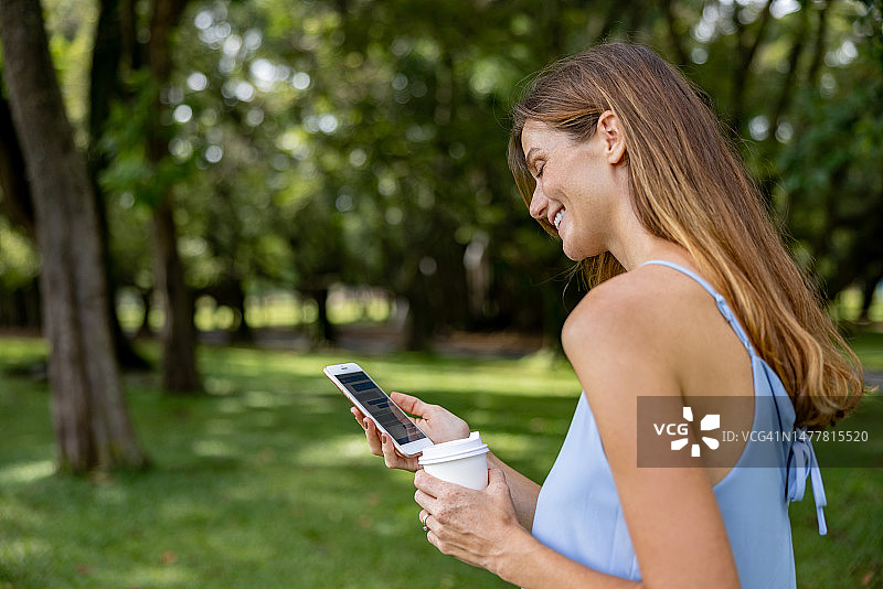 一名女子在公园边喝咖啡边玩手机图片素材