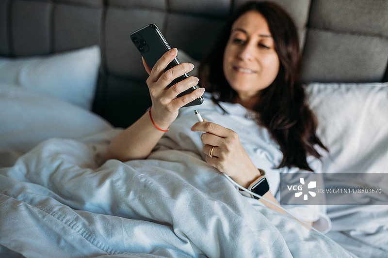 女子躺在床上时将充电线插入智能手机图片素材