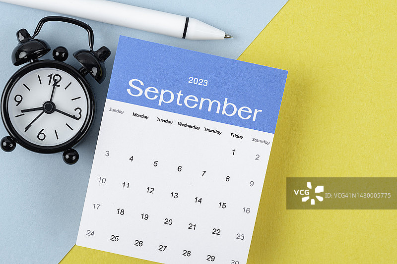日历桌2023:9月是组织者用闹钟和白笔在双色纸背景上做计划和截止日期的月份。图片素材