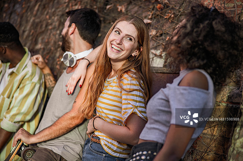 快乐的红发女人靠着墙和她的朋友聊天。图片素材