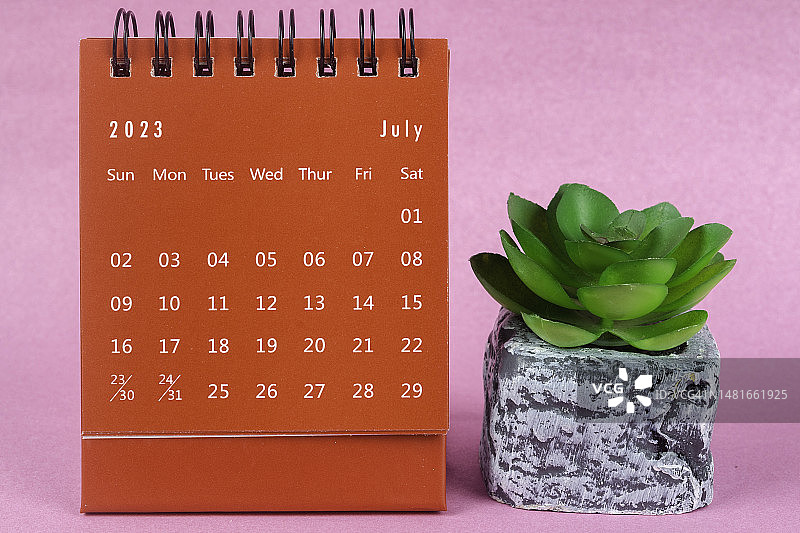 日历桌2023:7月是组织者计划和截止日期的月份，在粉红色的纸背景下放置室内植物。图片素材