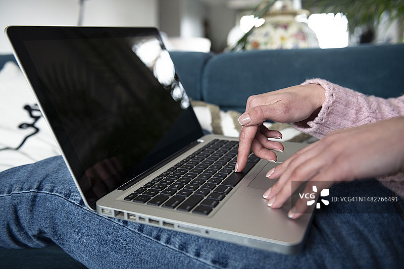 一位女士坐在家里的沙发上，用空白屏幕的笔记本电脑工作和打字图片素材