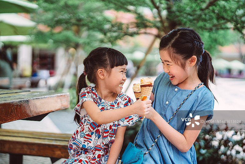 可爱开朗的妹妹在公园里玩的时候用他们的冰淇淋甜筒欢呼图片素材