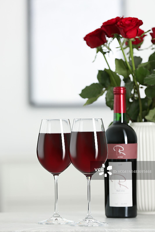 在房间的桌子上有一瓶、几杯红酒和一个插着玫瑰花的花瓶。浪漫的约会图片素材