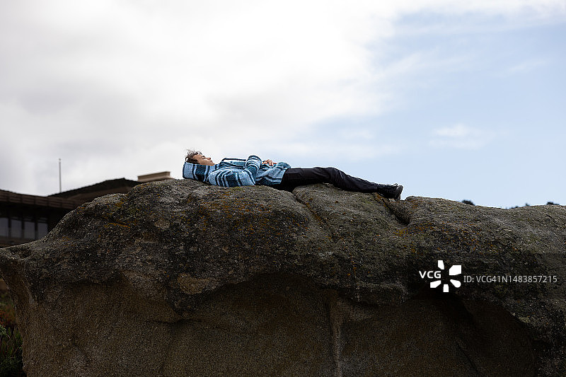 穿着巴哈帽衫的少年躺在一块巨石上图片素材