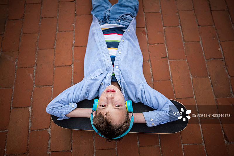 一个十几岁的男孩躺在滑板上，头上戴着耳机图片素材