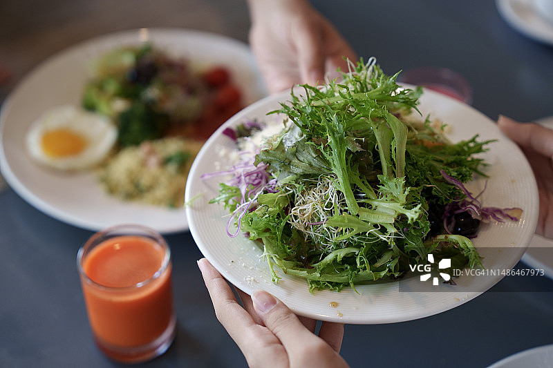一个家庭在早餐时分享新鲜的蔬菜沙拉，突出了食物共享和外出就餐的概念。图片素材