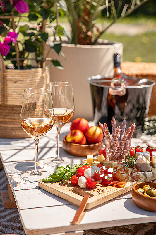 玫瑰色酒杯配上开胃菜野餐食品和小吃，放在阳光明媚的花园聚会桌上图片素材