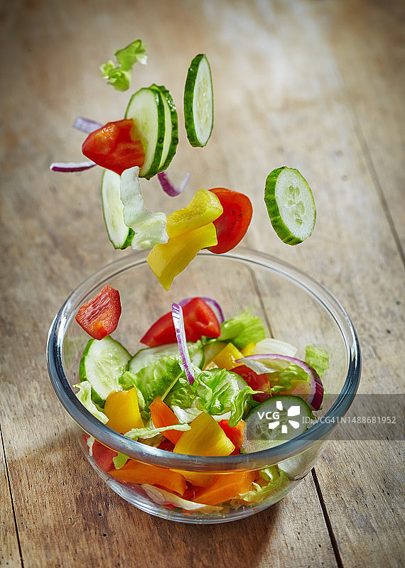 新鲜的蔬菜掉进木桌上的玻璃碗里图片素材
