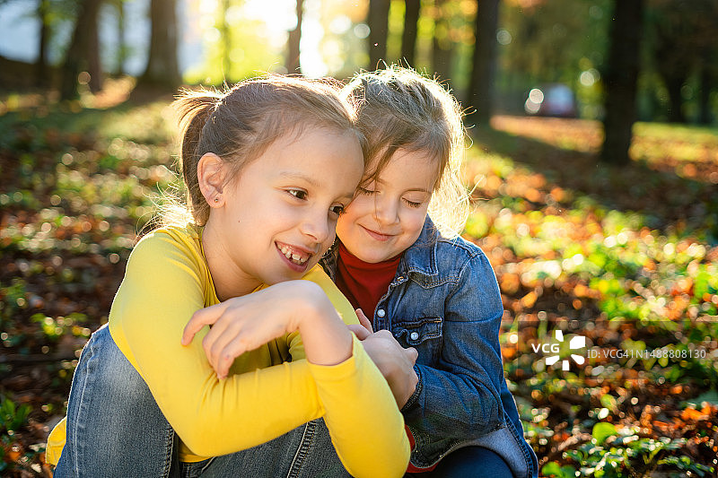 两个可爱的女孩在秋天的公园里拥抱图片素材