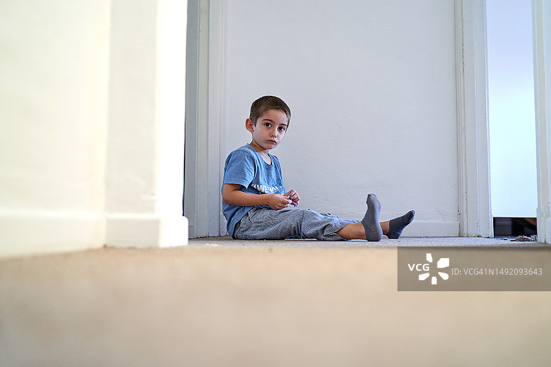 一个小男孩坐在走廊的地板上图片素材