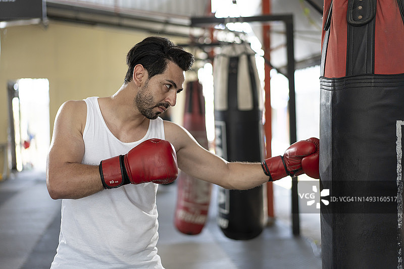 年轻英俊的男拳击手，肌肉发达，戴着红手套在健身房训练图片素材