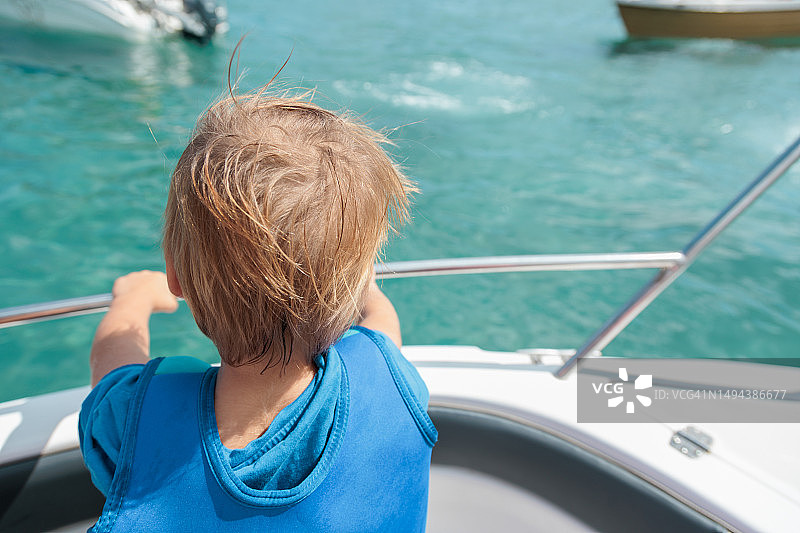 家庭海上冒险。身穿救生衣的小男孩(3-4岁)在私人船上观看海洋生物的后视图。图片素材