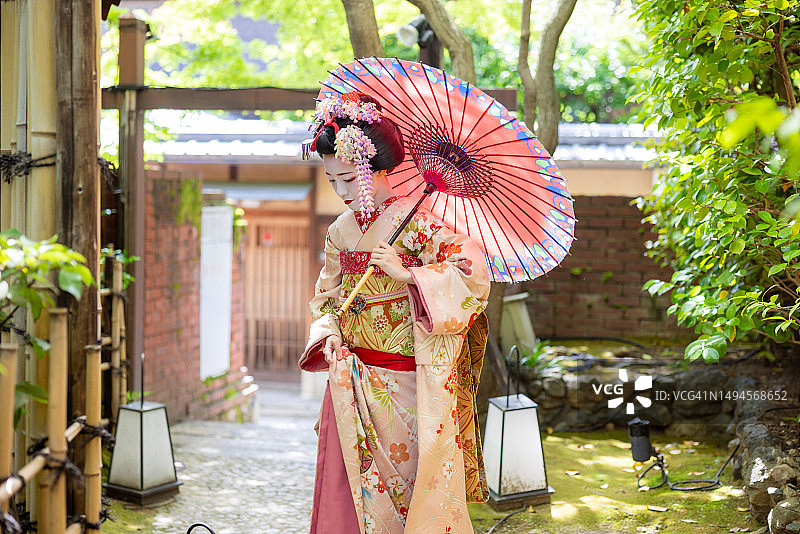 日本艺妓站在京都祗园狭窄的小路上，用传统的日本纸伞遮阳图片素材