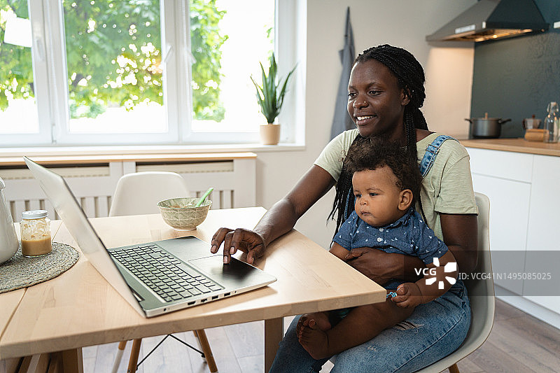 一位黑人母亲正在给她的儿子喂奶，而他正在用笔记本电脑看动画片图片素材