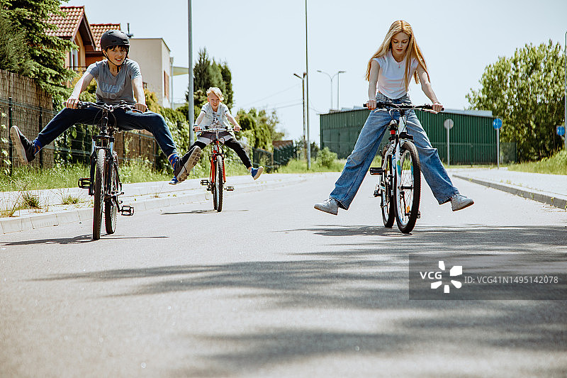 三个孩子在郊区的街道上骑自行车，把腿从踏板上抬起图片素材