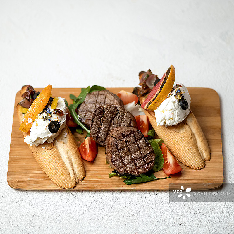 牛排，面包，奶酪和蔬菜放在木板上。烤肉上煎的肉配小菜。白色背景。前视图。本空间图片素材