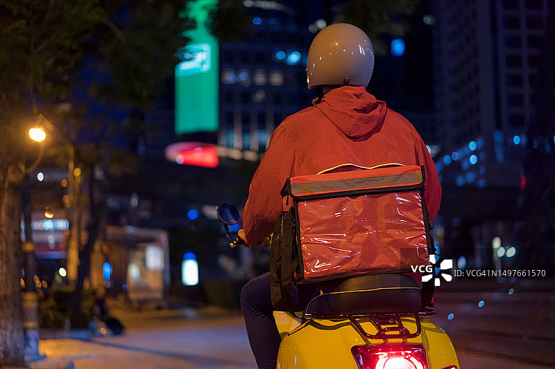 后视镜:快递员驾驶摩托车在夜晚穿过城市。图片素材
