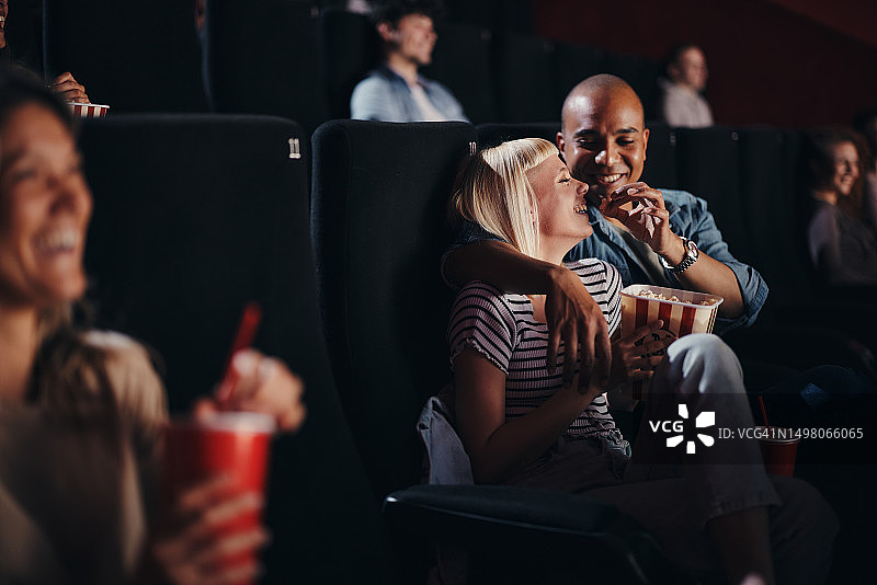 幸福的多元夫妻在电影院看电影时吃着爆米花。图片素材